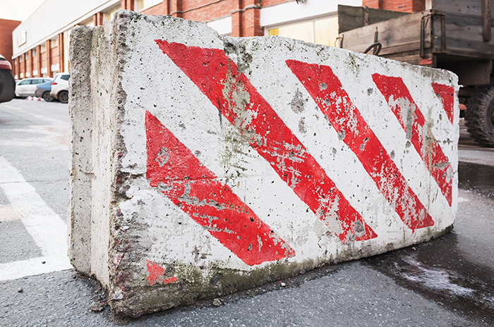 Close-up photo of concrete road block with warning red white diagonal striped pattern
