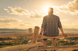 Man sitting on wooden fence and looking at sunrise